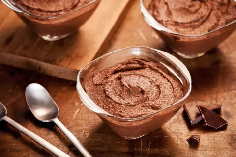 Delicioso mousse de chocolate en copas de cristal, listo para disfrutar. Trozos de chocolate negro al lado.
