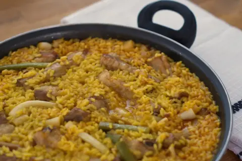 Paella recién hecha, un plato perfecto para tus recetas de arroz. Con trozos de carne, judías verdes y un arroz amarillo vibrante.