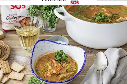 Un delicioso arroz con bogavante, servido en un cuenco con perejil fresco. A su lado, galletas saladas y una copa de vino blanco.