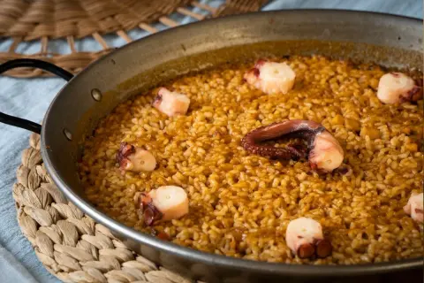 Arroz con pulpo en paellera, con trozos de pulpo bien visibles entre el arroz dorado.