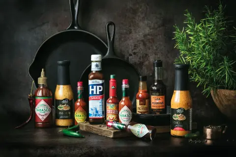 Variedad de salsas para carnes, incluyendo Tabasco, HP Sauce y Lea & Perrins, junto a chiles y romero.