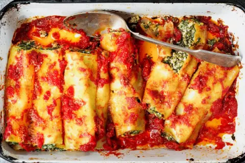 Canelones de atún horneados con salsa de tomate y espinacas, listos para servir en una bandeja.
