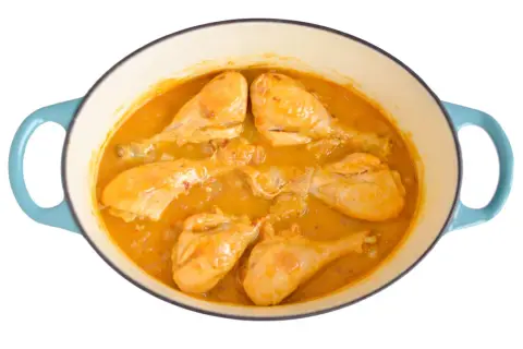 Pollo en salsa dorada, cocinándose en una olla azul. Las piezas de pollo están tiernas y cubiertas de una rica salsa.