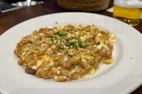 Delicioso revuelto de bacalao con trocitos de frutos secos y perejil picado, servido en plato blanco.