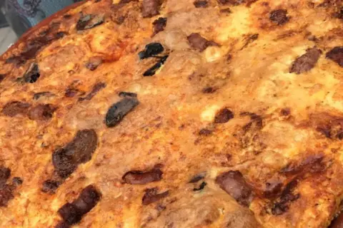 Arroz con costra dorado y crujiente, con trozos de carne y aceitunas negras incrustados.