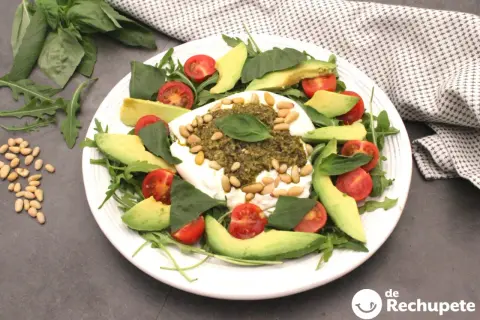 Deliciosa ensalada de burrata y pesto, con aguacate, tomates cherry y piñones.