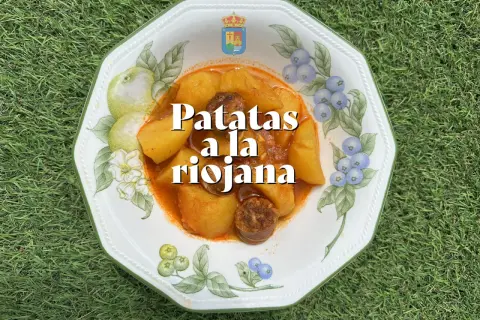 Un plato de patatas a la riojana, con trozos de chorizo y patata en una salsa rojiza, servido en una vajilla decorada con frutas y bayas.