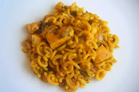 Fideuà de pollo con fideos rizados y trozos de pollo en salsa dorada, servida en plato blanco.