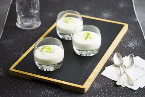 Tres vasitos de cremoso mousse de limón, decorados con ralladura verde, listos para disfrutar.