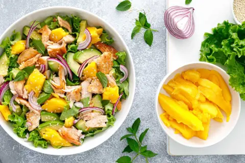 Ensalada de mango con salmón desmenuzado, aguacate, cebolla morada y hojas verdes. ¡Una explosión de sabor!