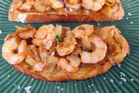 Tostadas con gambones al ajillo, cubiertas de ajo y perejil, espolvoreadas con sal marina gruesa sobre un plato verde.