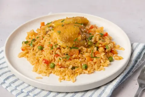 Un plato de arroz con pollo, guisantes, zanahoria y pimiento rojo, adornado con perejil picado.