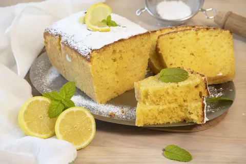 Un delicioso bizcocho de limón, espolvoreado con azúcar glas y decorado con rodajas de limón y hojas de menta.
