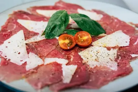 Delicado carpaccio de ternera con lascas de parmesano, hojas de albahaca y tomates cherry.