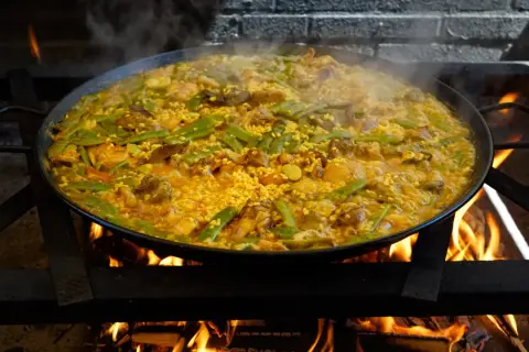 Arroz con carne humeante en paellera sobre fuego vivo. Judías verdes y trozos de carne se mezclan con el arroz dorado.