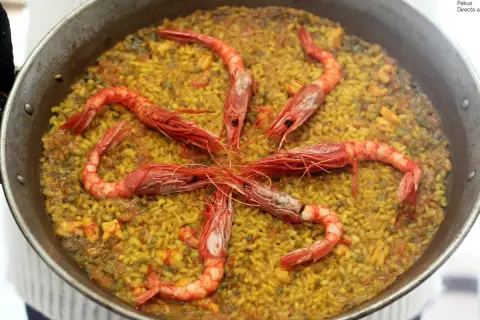 Arroz con carabineros, un plato de paella con gambas rojas grandes dispuestas en círculo sobre el arroz amarillo.