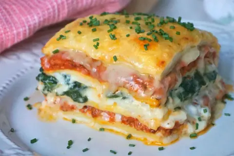 Porción de lasaña de espinacas, con capas de pasta, salsa de tomate, queso derretido y espinacas, espolvoreada con cebollín.