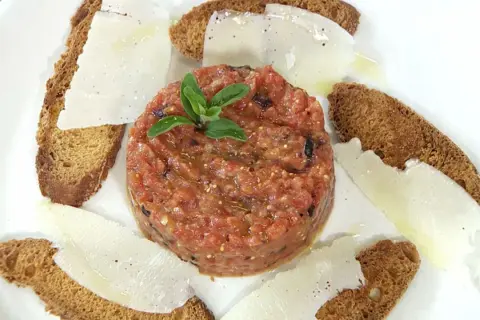 Tartar de tomate fresco, servido con finas láminas de queso y tostadas crujientes. Un bocado ligero y lleno de sabor.