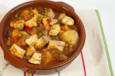 Un delicioso marmitako de salmón, con trozos de pescado, patatas, guisantes y pimientos rojos en una cazuela de barro.