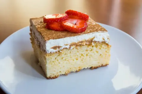 Un trozo de tarta 3 leches, esponjoso y cubierto con crema batida, canela y fresas frescas.