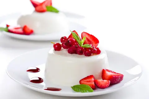 Deliciosa panna cotta receta, decorada con fresas, grosellas rojas y menta.
