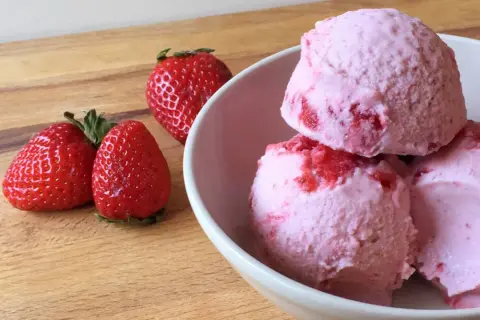 Bol con helado de fresa cremoso y trozos de fruta fresca.