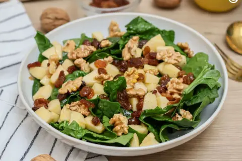 Deliciosa ensalada de espinacas con trozos de manzana, pasas y nueces. Una combinación crujiente y dulce.