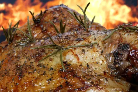 Pierna de cordero al horno, dorada y jugosa, con romero y especias, sobre un fondo de llamas. ¡Un festín irresistible!