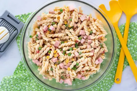 Ensalada de pasta con jamón, guisantes y maíz, lista para servir con su salsa para ensalada de pasta.