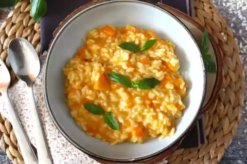 Cremoso risotto de calabaza, adornado con hojas de albahaca fresca, servido en un cuenco rústico.