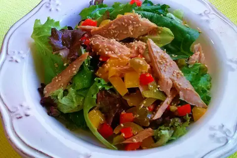Ensalada de ventresca con pimientos de colores y semillas de sésamo, servida sobre hojas verdes frescas.