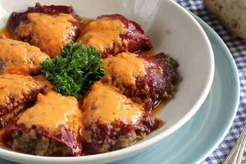 Pimientos rellenos de carne cubiertos con una cremosa salsa, decorados con perejil fresco.