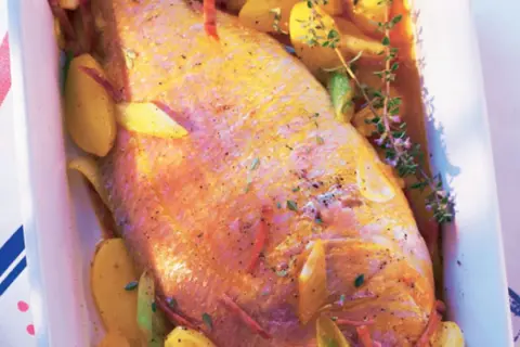 Pescado rosado al horno con patatas y hierbas aromáticas en una bandeja blanca.