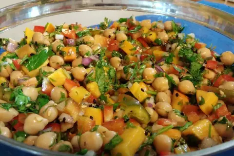 Ensalada de legumbres vibrante con garbanzos, pimientos de colores, cebolla morada y cilantro fresco, todo mezclado en un bol de vidrio.