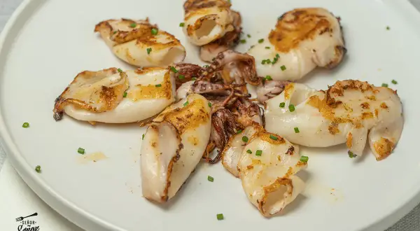 Deliciosos chipirones a la plancha, dorados y tiernos, servidos en un plato blanco con cebollino picado.