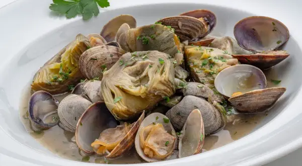 Delicioso plato de alcachofas con almejas, un manjar marino y vegetal en una salsa suave.