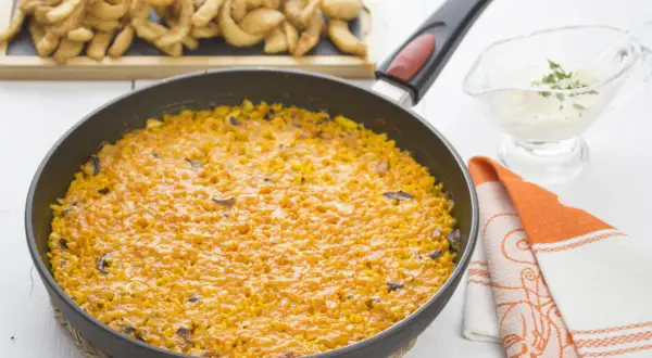 Arroz con sepia en paellera, acompañado de patatas fritas y una salsa cremosa.