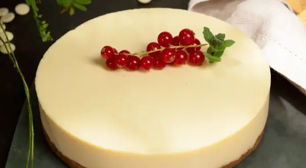 Deliciosa tarta de chocolate blanco, coronada con grosellas rojas y menta fresca. Un postre elegante y cremoso.