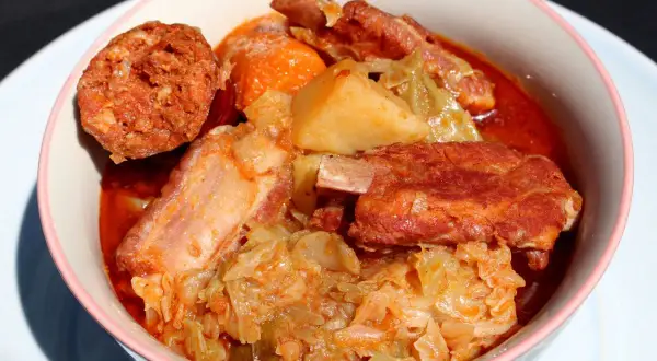 Un reconfortante plato de patatas con costillas, repollo y chorizo en un cuenco rosa.