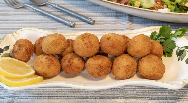 Croquetas de pollo doradas y crujientes en una bandeja decorada, acompañadas de rodajas de limón y perejil.