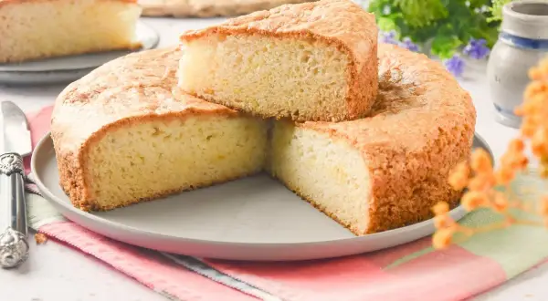 Bizcocho sin huevo esponjoso y dorado, cortado en porciones sobre un plato gris. Ideal para desayunos o meriendas.