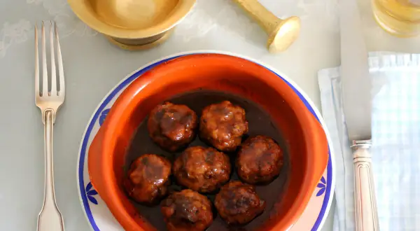 Un cuenco de barro con deliciosas albóndigas en salsa, listo para ser disfrutado con tenedor y cuchillo.