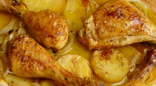 Pollo al horno con patatas y cebolla, dorado y jugoso, con hierbas aromáticas. Un plato casero irresistible.