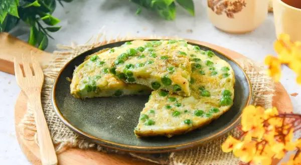 Tortilla de guisantes recién hecha, con trozos de patata y guisantes verdes, servida en un plato oscuro.