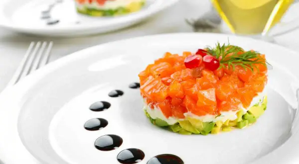 Delicioso tartar de salmón con aguacate, coronado con granada y eneldo. Un plato elegante con un toque de salsa balsámica.