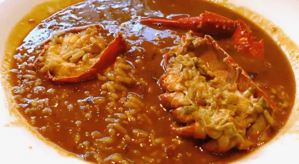 Delicioso arroz caldoso de marisco con trozos de langosta en un plato blanco.