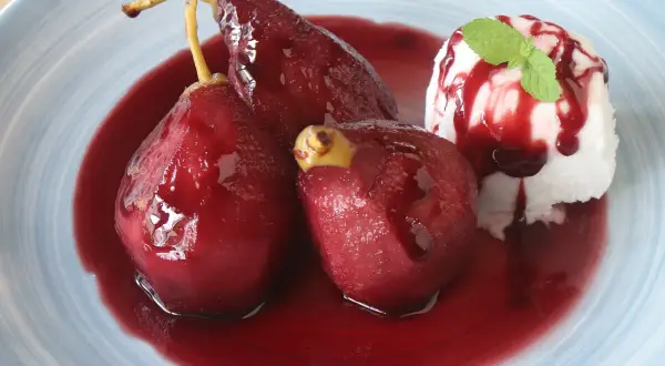 Peras al vino, tiernas y brillantes, bañadas en su jugo rojo, acompañadas de helado y menta.