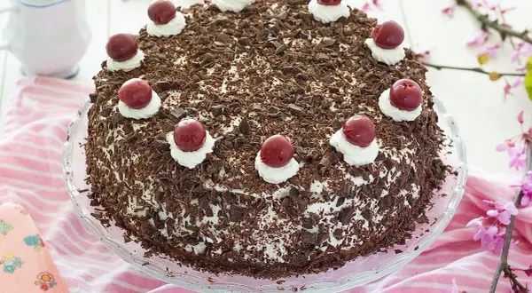 Deliciosa tarta Selva Negra, cubierta de virutas de chocolate y coronada con cerezas y nata. Perfecta para cualquier celebración.
