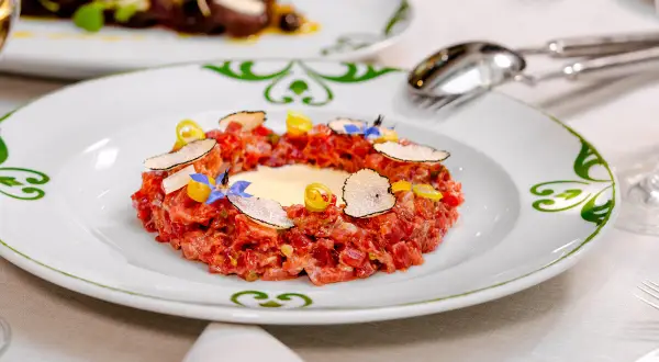 Delicioso tartar de atún fresco, adornado con láminas de trufa negra, flores comestibles y un toque de limón.