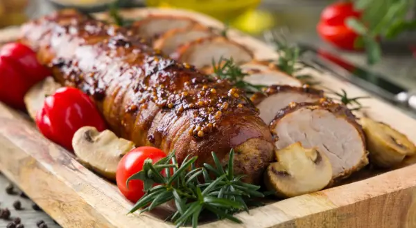 Lomo de cerdo al horno jugoso, glaseado y especiado, servido con champiñones, pimientos rojos y romero en tabla de madera.
